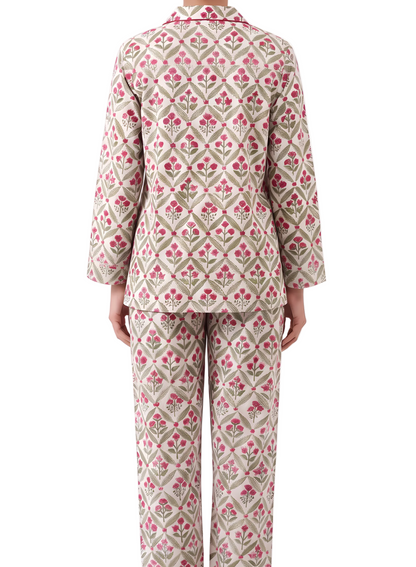 A person shown from the back wearing a matching two-piece pajama set with a beige base and a repeating pink and green floral diamond pattern, photographed against a plain white studio background.